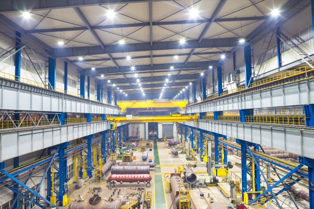 Grote industriële fabriekshal met zware machines, pijpen en kranen onder helder verlichting